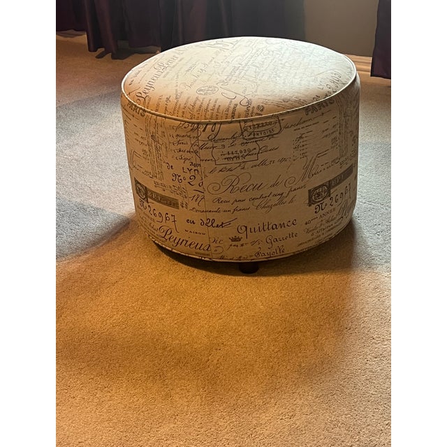 This French script ottoman is upholstered in a neutral fabric, generally described as off-white, beige, or cream, with...