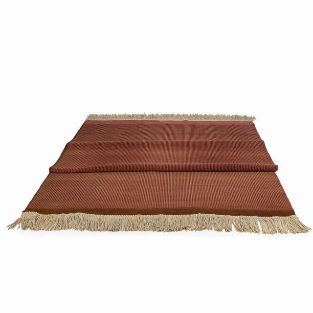 A simple rug made in the fifties. The shade of the rug is brown with longitudinal stripes. There are typical fringes on...