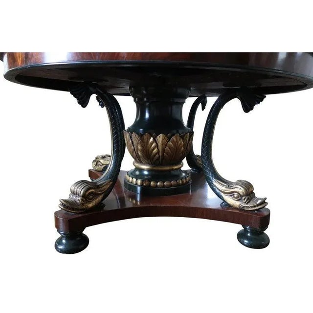 19th-century Mahogany center table with finely carved gilt dolphin base, ebony black bun feet, and ebony and gilt center...