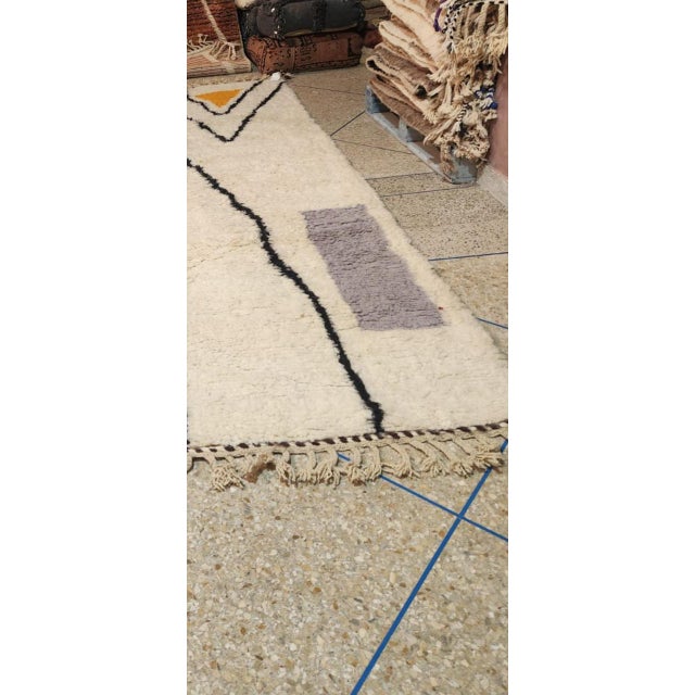 This handmade Moroccan rug features a modern and minimalist geometric design, crafted with a soft ivory background and...