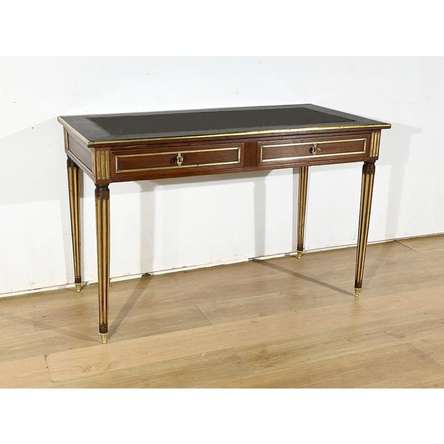 Louis XVI style mahogany veneer flat desk, with a miter-cut framed top whose edge is molded with brass strips. The center...