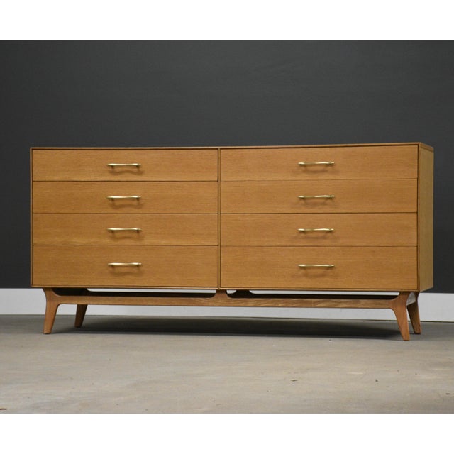A mid century modern oak long eight drawer dresser with canted legs and polished brass drawer pulls made by RWAY...
