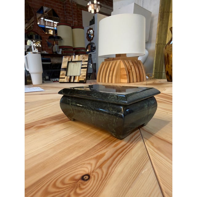 Decorative rectangular box in polished deep green marble, featuring intricate veining and subtle variations in tone. Its...