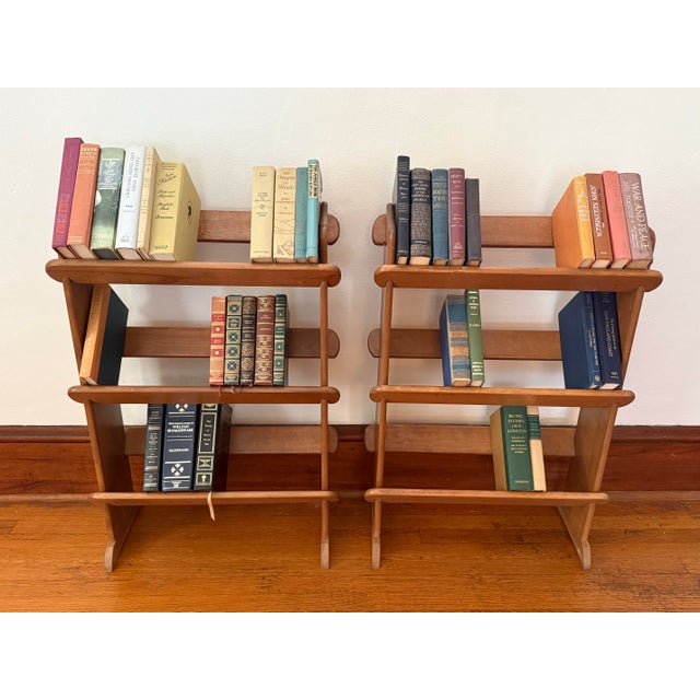 A vertical three-tier wooden book rack with angled trough shelves, dowel backs, tapered side panels, and a dark oak-like...