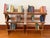 A vertical three-tier wooden book rack with angled trough shelves, dowel backs, tapered side panels, and a dark oak-like...