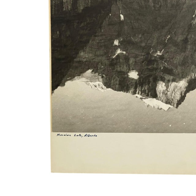Vintage black and white photographic print depicting Moraine Lake in Banff National Park, Alberta, Canada. The composition...