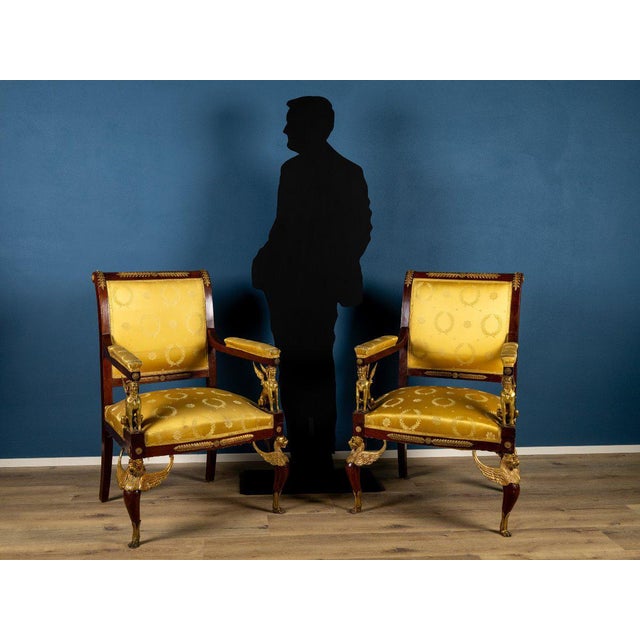 An elegant pair of Empire-style armchairs, crafted in the early 19th century, featuring a stately silhouette and refined...