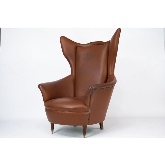 Beautiful mid-century wingback armchair manufactured in Italy in the 1950s. This elegant piece features a sculptural high-...