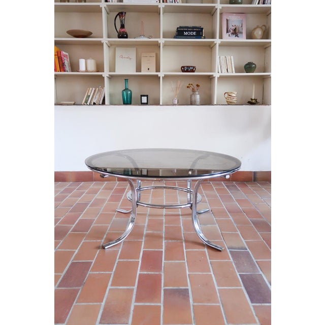 A round 1970s coffee table with a tubular chrome base and a smoked glass top, pure Space Age in its logic: the metal does...
