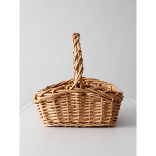 A vintage handwoven gathering basket in a light natural tone, shaped with a softly squared form and a thick, twisted...