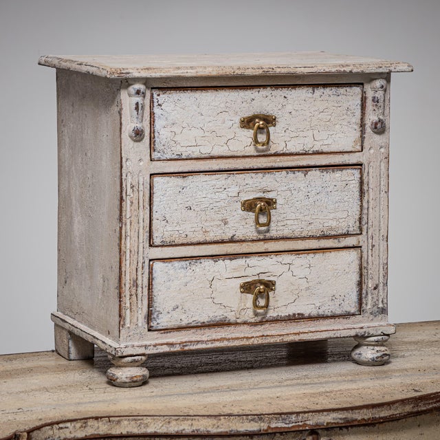Miniature commode with three drawers, fluted pilasters, and compressed bun feet. The drawers feature brass pull handles....