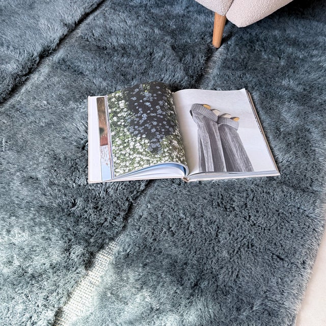 A quietly textured slate grey rug, its plush surface subtly divided by fine vertical lines into soft, uneven panels. The...