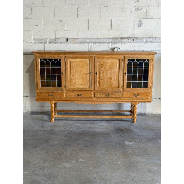 This oak sideboard in style of Henning Kjærnulf stands on turned legs with double stretchers. Two stained glass outer...