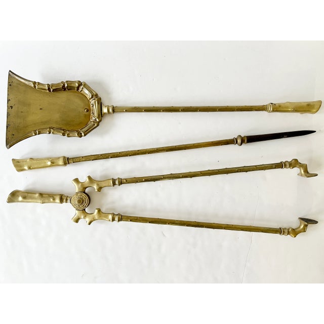A set of three Hollywood Regency cast brass fireplace tools, circa 1920s. Each piece features a wooden branch texture on...