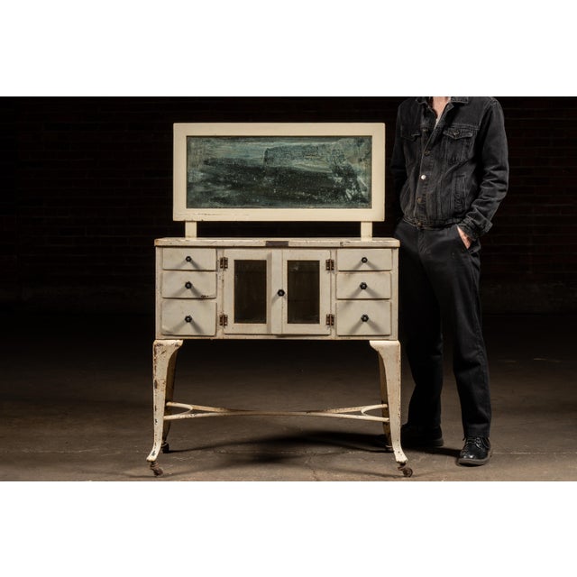 An antique medical cabinet complete with attached original mirror on casters. This cabinet is finished in an antique white...