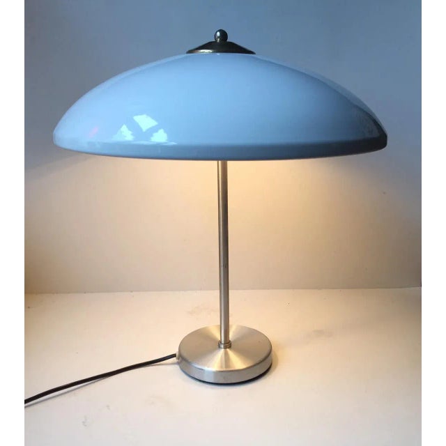 This large table lamp with a white enameled shade and brass accents sits on a brushed aluminium base. It was designed by...