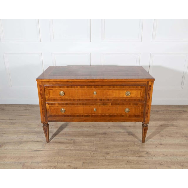 A refined neoclassical chest of drawers in walnut and cherry, distinguished by its rich inlay work and balanced...