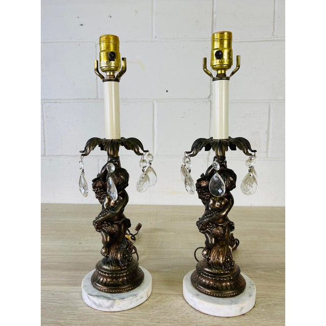 Vintage 1950s pair of metal cherub designed table lamps with glass prisms and marble bases. The lamps are wired for the US...
