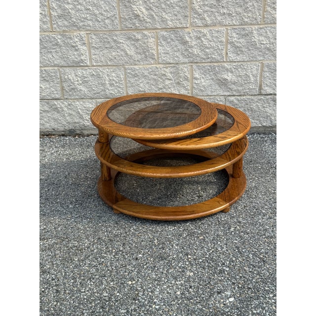 This 1970s coffee table pairs a warm oak frame with three circular smoked glass tops arranged in a tiered, expandable...