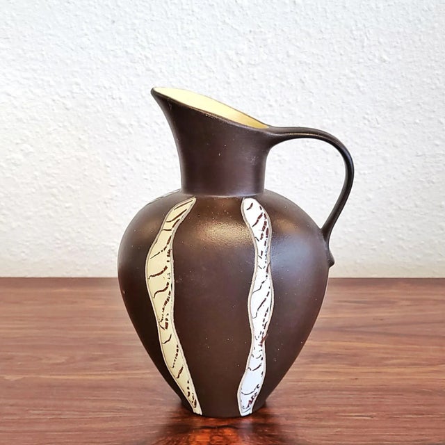 A compact pitcher vase with a classically inspired profile (model Nr. 2205/21). Glossy stripes of glaze in alternating...