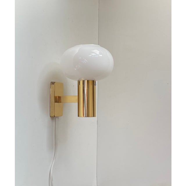 An elegantly crafted wall sconce in brass featuring a mushroom shaped white opaline glass shade. Unknow Scandinavian...