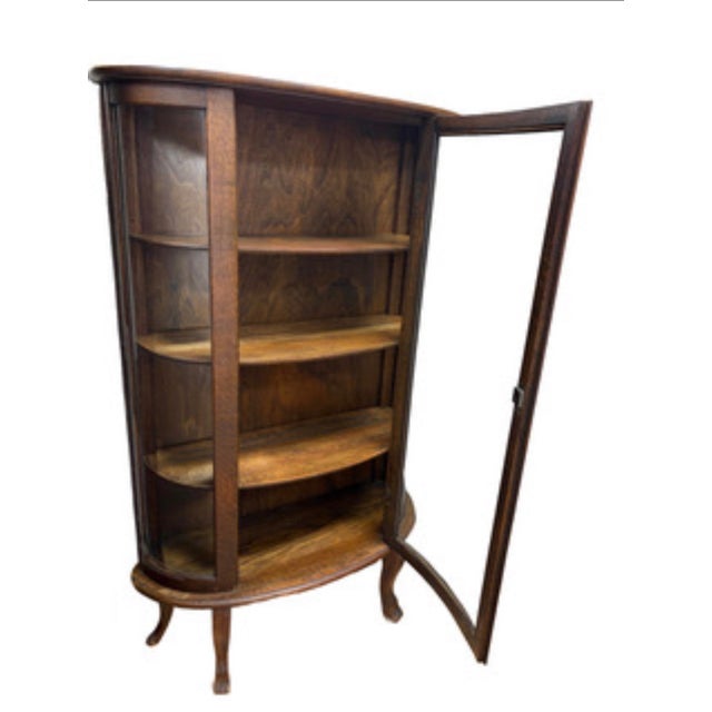 An antique curved-glass curio cabinet retaining its original glass and finish, offering an elegant way to display...