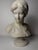 A 19th-century sculpture depicting the half-length figure of a young woman. We note a serene facial expression, almost a...