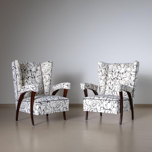 Pair of Italian lounge chairs with trapezoidal, large backrests and upholstered armrests. The armchairs stand on tapered,...