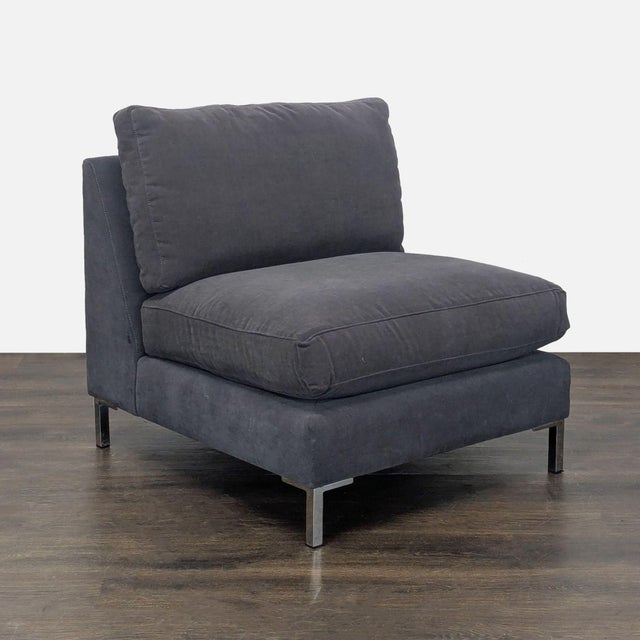 This CB2 lounge chair features a modern armless design and is upholstered in a dark gray fabric. It has plush cushions for...