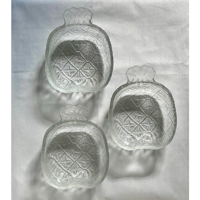 A set of three pressed glass dishes in the shape of pineapples with stems as handles.