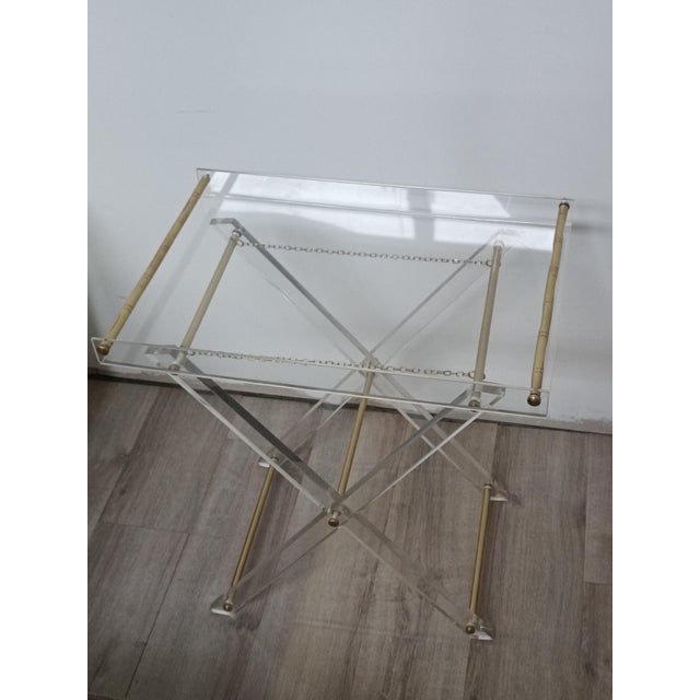 Beautiful folding side table. Italy, 1970s. Acrylic glass frame. Brass details, tubes, and chains. The X-shaped base...
