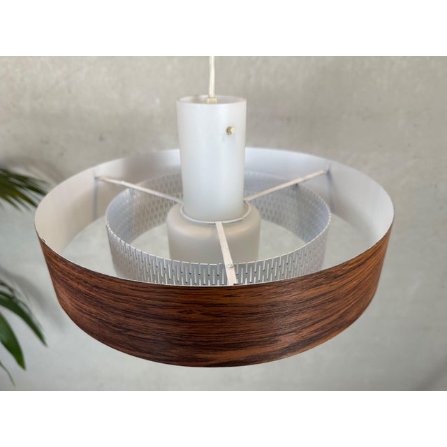 Vintage Scandinavian pendant lamp. Metal outer ring with rosewood grain and perforated inner ring. The whole is supported...