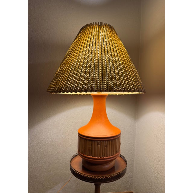 Vintage 1970s table lamp with a textured burnt-orange ceramic body, natural bamboo or split-reed banding, and a wood base....