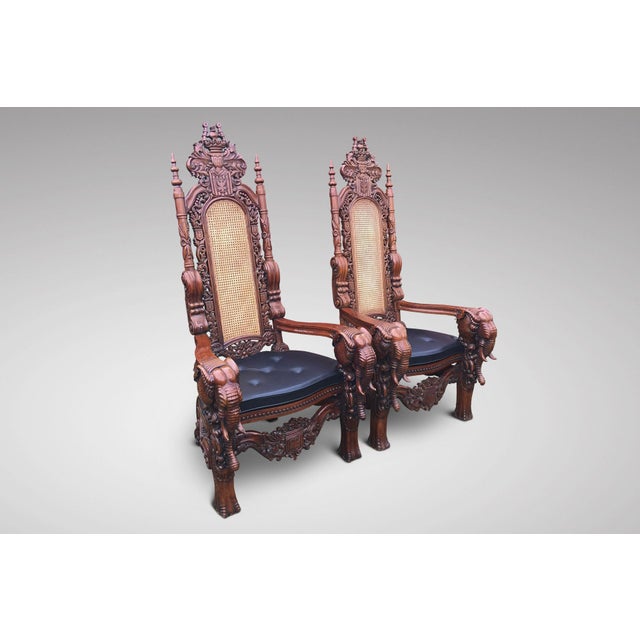 A pair of impressive carved walnut elephant high backed Throne Armchairs, cane back and seat rest, with a fitted black...