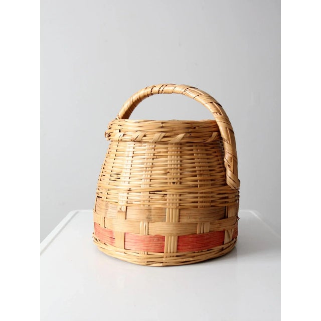 This is an antique woven basket. The hand-woven basket features a pink stripe around the base, a fitted lid, and short...