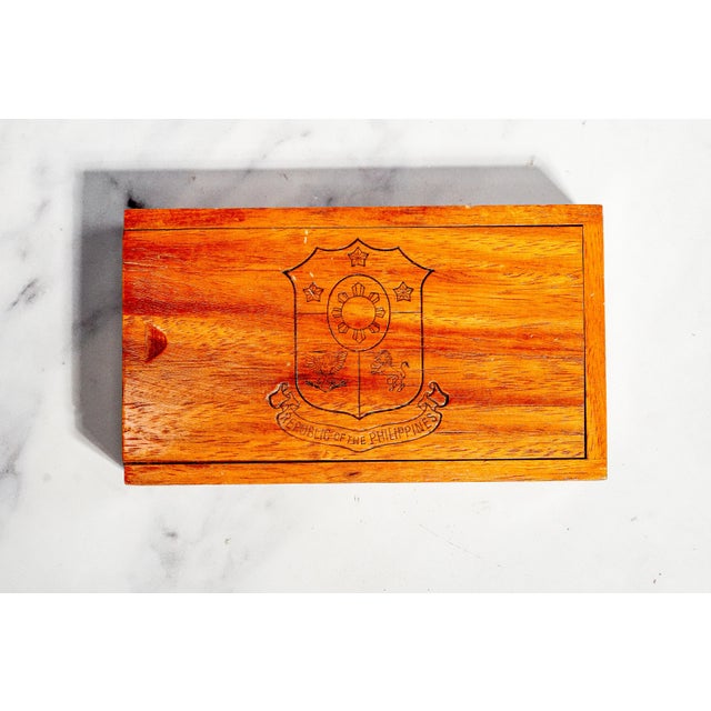 A handsome vintage wooden cigar box featuring the coat of arms of the Republic of the Philippines, combining traditional...