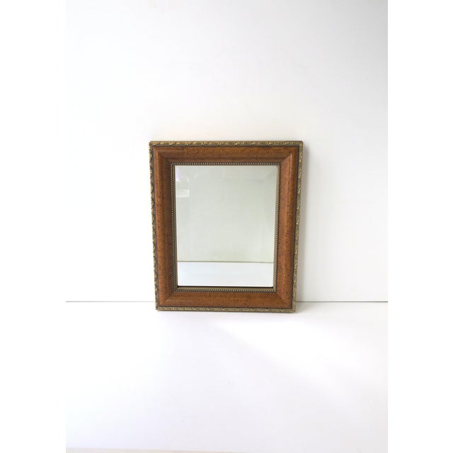 A relatively small, beveled wall mirror with a burl‑style wood frame, late 20th century. The frame features a warm brown...