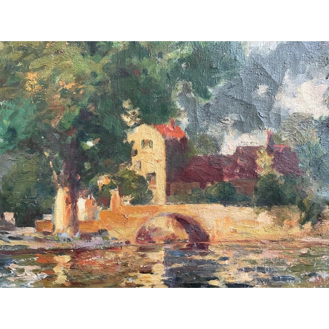 Stunning painting of a quaint bridge, building, and lush trees with dappled sunlight at the edge of a lake. Rich patina...