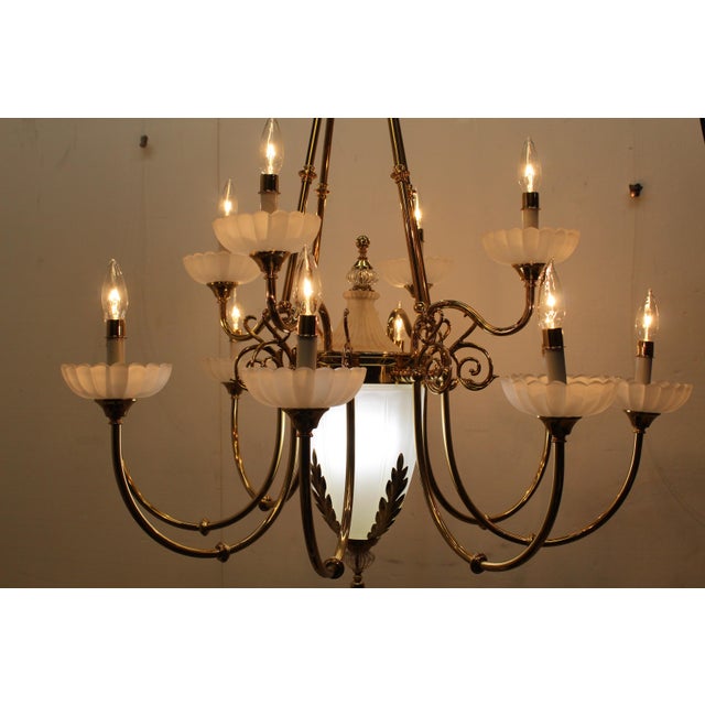 Brass 12 arm chandelier has frosted glass bobeches and a large, urn-shaped frosted center glass surrounded by laurel...