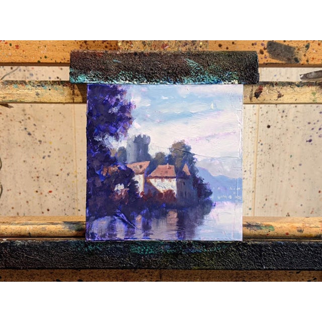 This oil painting captures a serene lakeside scene featuring a charming chateau nestled among lush trees, reflecting...