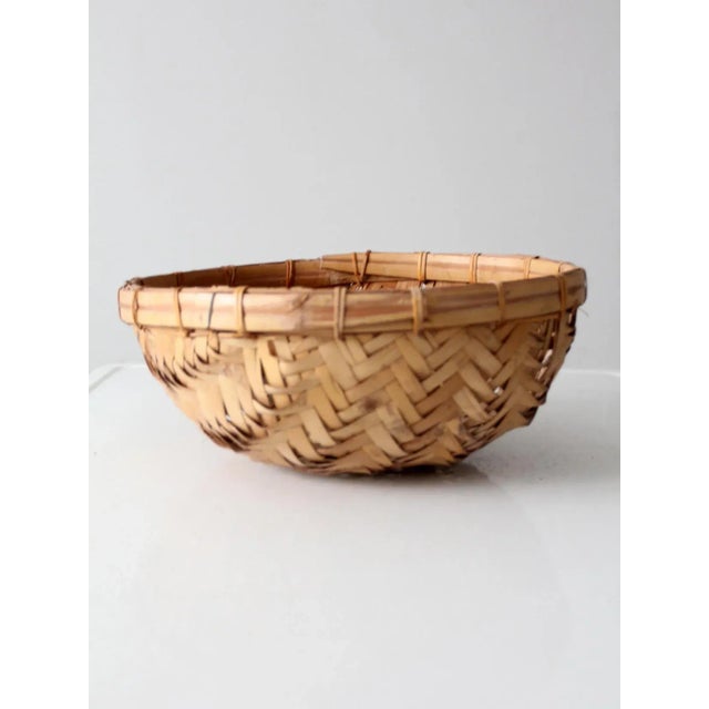 A vintage woven rattan basket bowl with a natural honey-toned finish and a herringbone-style weave. Light in form yet...