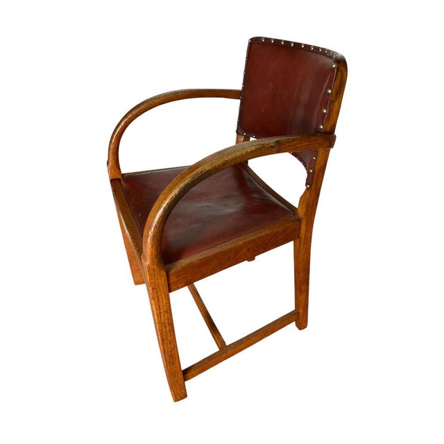 A vintage art deco-style armchair, characterized by its robust wooden frame and dark brown leather upholstery. The chair...