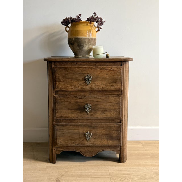 An early 19th-century walnut commode with three graduated drawers, each framed in simple molding and fitted with its...