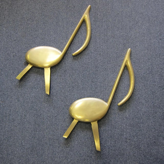 A Pair of mid century modern solid brass musical note fireplace andirons with back fasteners to secure log holder supports...