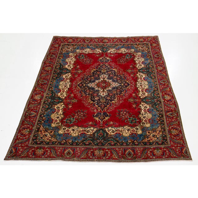 This vintage handmade Persian Tabriz wool rug features a striking red background adorned with a vibrant rosette motif and...