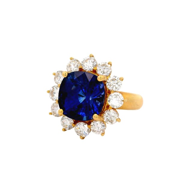 A captivating ring featuring a deep blue cushion sapphire weighing 7.11 carats, set prominently at the center. Encircling...