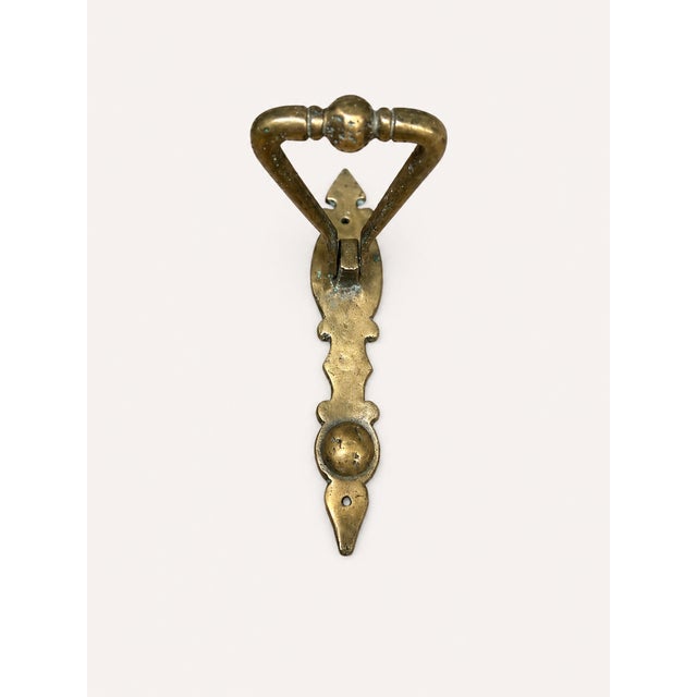 A striking antique solid brass door knocker featuring a bold triangular ring design mounted on an elongated decorative...