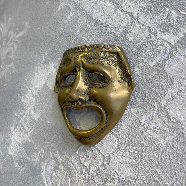 This decorative brass wall mask evokes the celebrated style of classical greco-roman theater. This vintage piece captures...