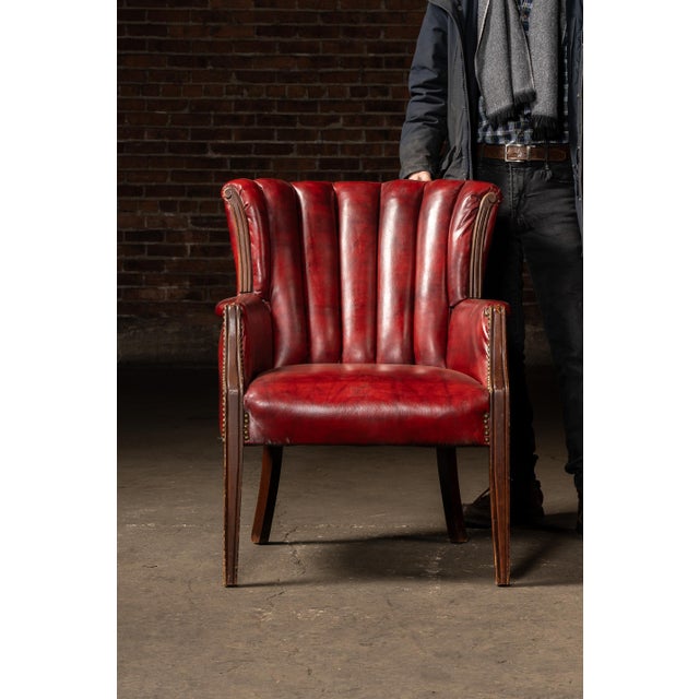 Compact leather armchair upholstered in deep oxblood red hide, featuring a vertical channel-back design that gives the...