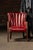 Compact leather armchair upholstered in deep oxblood red hide, featuring a vertical channel-back design that gives the...
